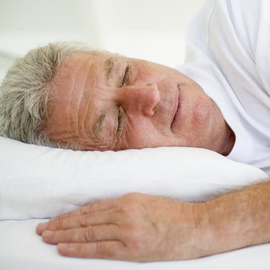 The old man wearing a white t-shirt and sleeping on a bed with white cushion