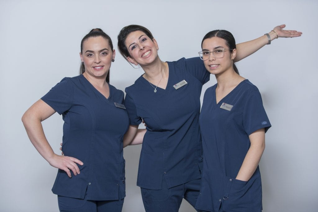 An image of three wise dental nurses standing next to each other with smiles on their faces.