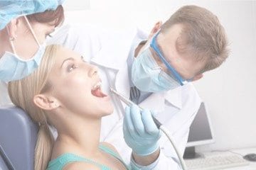 Dentist wearing mask on the face and checking patient's teeth with dental equipment and nurse beside